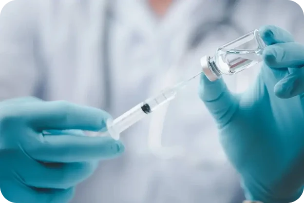 A gloved hand drawing a vaccine into a syringe from a vial