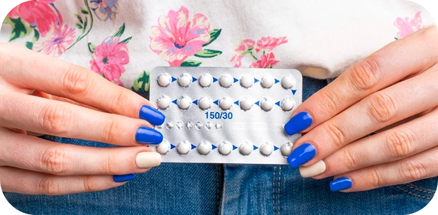 Hands holding a blister pack of contraceptive pills against a floral top and jeans