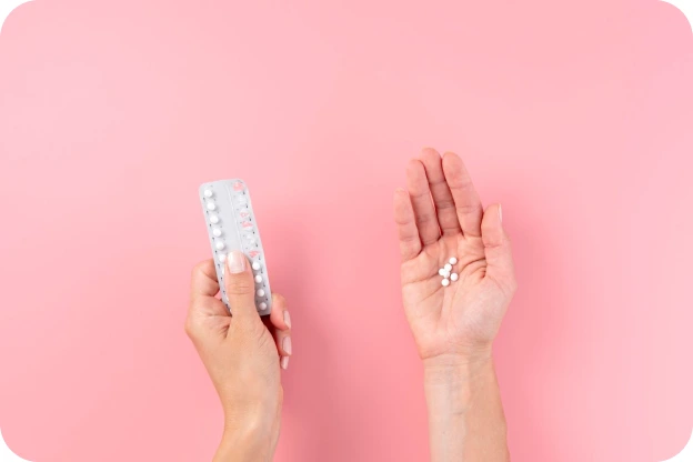 A hand holding a blister pack of pills beside a hand holding two white tablets, on a pink background