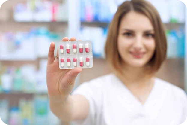A smiling pharmacist holding up a blister pack of red and white capsules